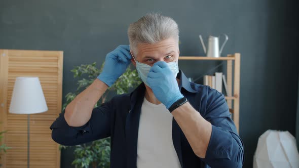 Slow Motion of Handsome Man Putting on Medical Face Mask at Home Looking at Camera alt