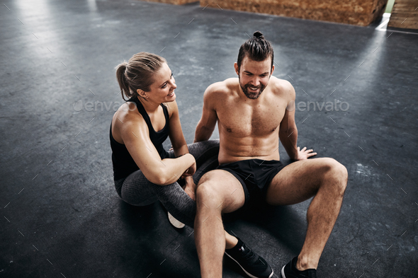 Two fit young people sitting together on a gym floor
