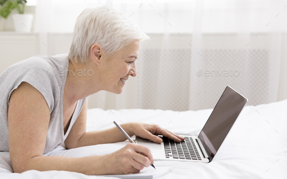 Cheerful skilled senior woman lying in bed
