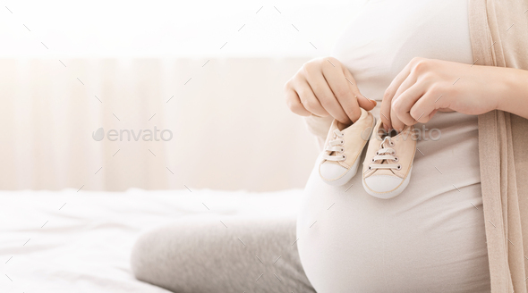 Small shoes for unborn baby on belly of pregnant woman