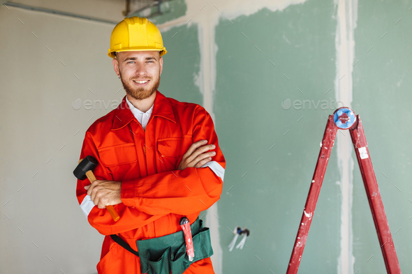 Smiling builder in orange work clothes and hardhat holding hamme