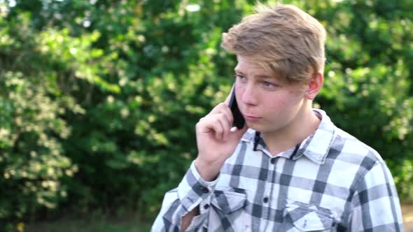 Young Caucasian Teenager Man in a Light Gray Checkered Shirt Speaks on the Phone alt