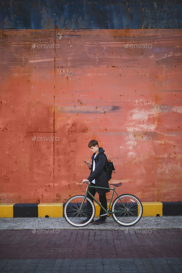 Guy with brown hair standing with bicycle and looking in cellphone - Stock Photo - Images