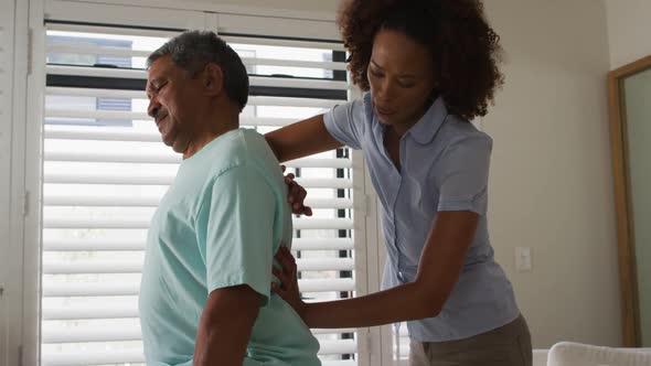 Mixed race female physiotherapist helping senior man massaging his back alt