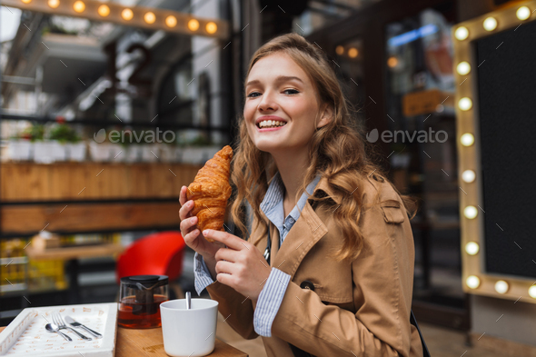 Young smiling woman in trench coat happily looking in camera hol - Stock Photo - Images