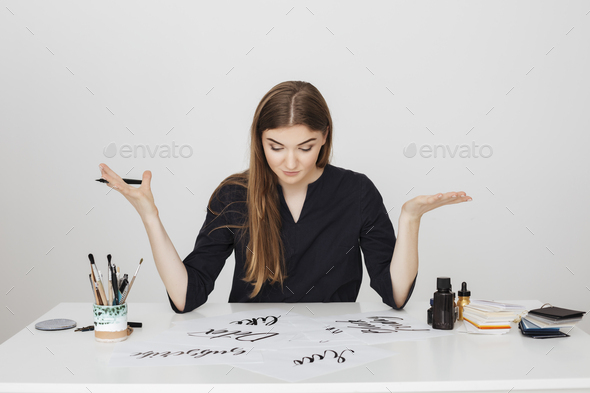 Young pretty lady sitting at the white desk with pen in hand and thoughtfully looking at papers