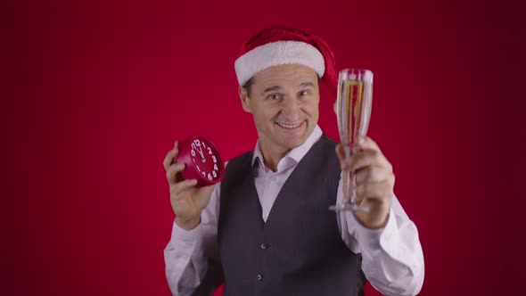 Cheerful Man in Santa Hat Holds Clock Drinking Champagne Seconds Before New Year