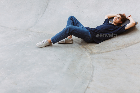 Young skater thoughtfully looking in camera while lying on skate