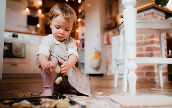 A small toddler girl making cakes on the floor in the kitchen at home.