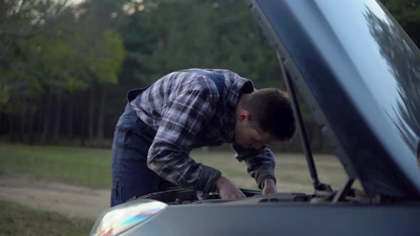 Mechanic Man in Uniform Open Hood Motor Fixing Broken Car on Forest Road