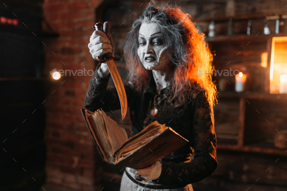 Scary witch holds spellbook and knife - Stock Photo - Images