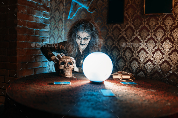 Scary witch with human skull over a crystal ball - Stock Photo - Images