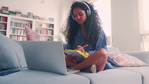 Young Indian Woman Student Listens to Online Lecture Sits on Sofa with Laptop alt