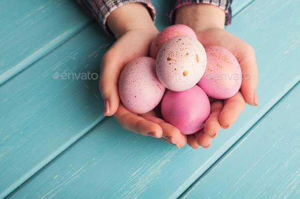 Woman holding pink colored easter eggs on blue table - Stock Photo - Images