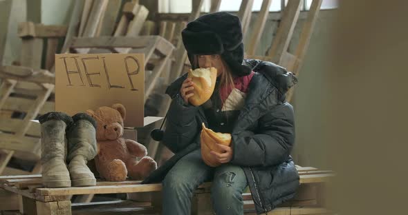 Portrait of a Homeless Girl with Dirty Face Eating Greedily the Loaf of Bread alt