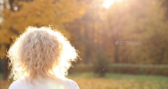 Beautiful blonde woman touching curly hair, walking in autumn park - Stock Photo - Images