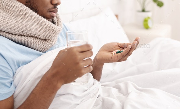 Young guy holding many pills, sitting in bed - Stock Photo - Images