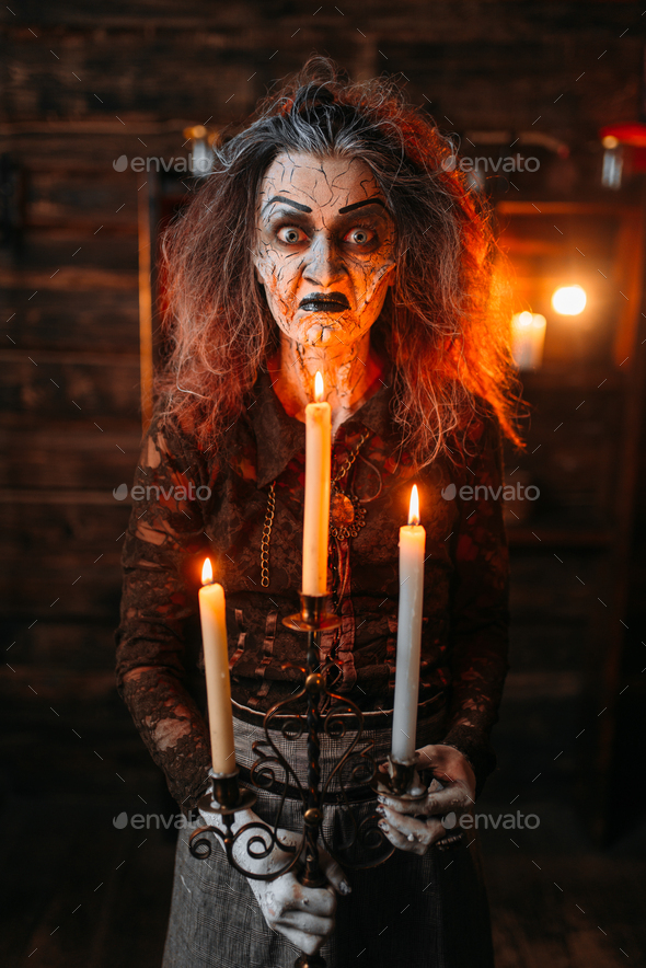 Scary witch with candlestick and cane reads spell - Stock Photo - Images