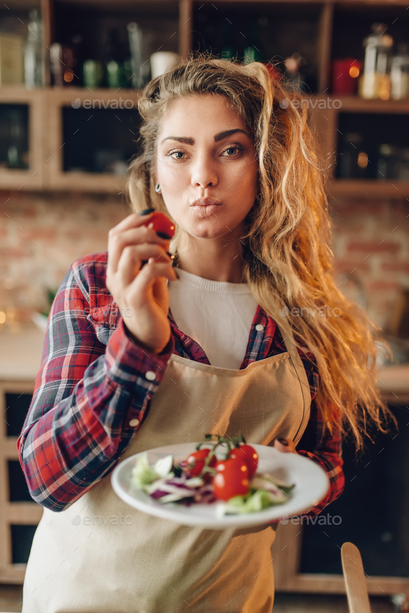 Smiling young housewife in apron prepares salad - Stock Photo - Images