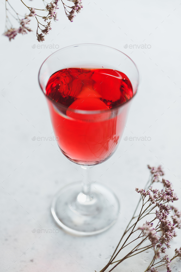 Glass of pink wine on a white table with flowers.
