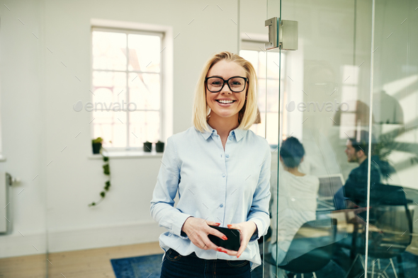 Smiling young businesswoman standing in a modern office - Stock Photo - Images