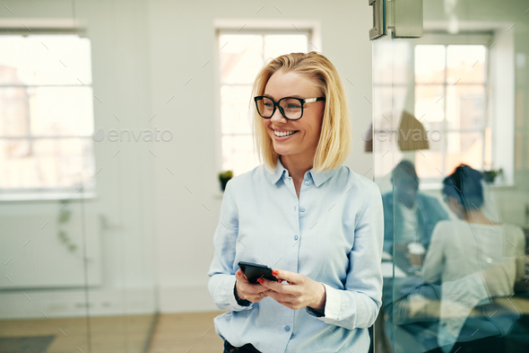 Laughing businesswoman standing in an office reading a text message