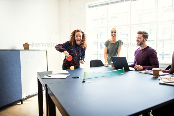 Laughing coworkers playing table tennis during their work break