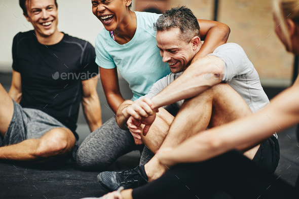 Diverse friends sitting in a gym laughing together after exercising