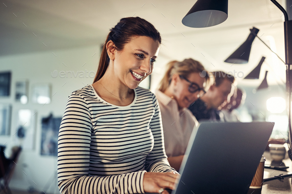 Smiling young designer working online at a table with coworkers