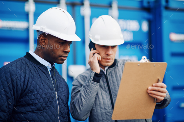 Engineers tracking inventory together in a commercial freight shipyard - Stock Photo - Images