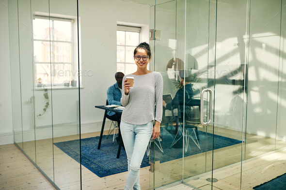 Smiling Asian businesswoman standing in an office enjoying a coffee - Stock Photo - Images