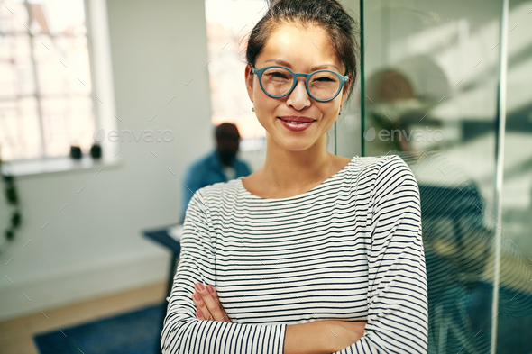 Smiling young Asian businesswoman standing in a bright office - Stock Photo - Images