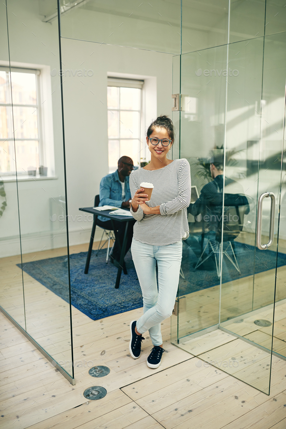Smiling Asian businesswoman drinking coffee in a modern office - Stock Photo - Images