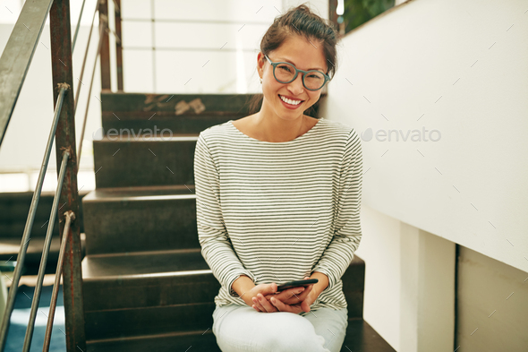 Smiling Asian businesswoman sitting on stairs reading a text message - Stock Photo - Images
