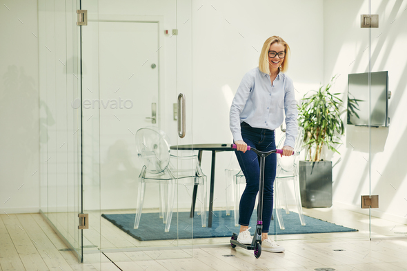 Laughing young businesswoman pushing a scooter around an office
