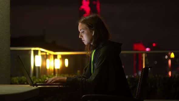 Young Woman Using Laptop on Balcony at Night