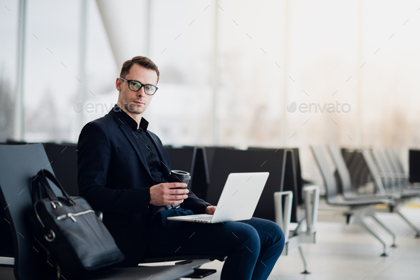 A business man sitting at the airport park working with his laptop and drinking takeaway coffee - Stock Photo - Images
