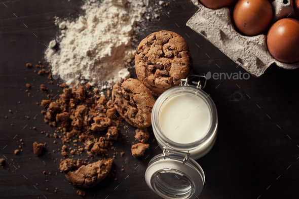 Top view of Homemade chocolate chip cookies with bottle of milk, white flour, fresh eggs and crumbs - Stock Photo - Images