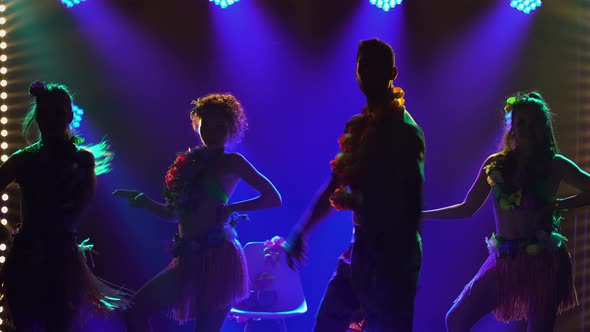 Silhouettes of Three Charming Women Dancing Around a Man Sitting on a Chair alt