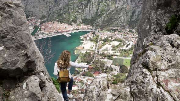 A Tourist Girl with a Backpack Stands on Top of a Mountain and Looks at the City