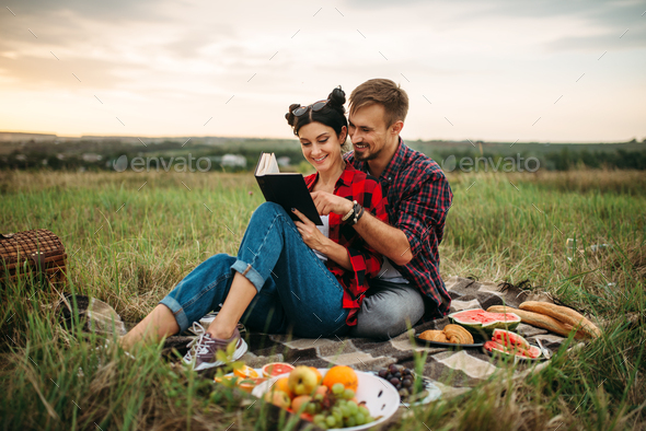 Couple reads book together, picnic in the field