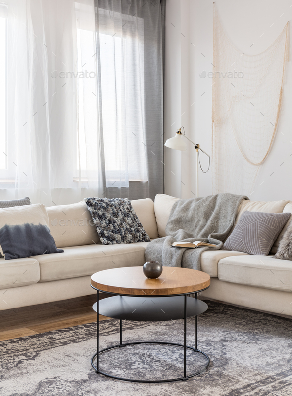 Round wooden coffee table in front of scandinavian corner sofa with pillows