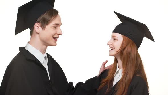 Ginger Caucasian Graduate Female Talking with Male in Black Robe and Square Academical Cap on White alt