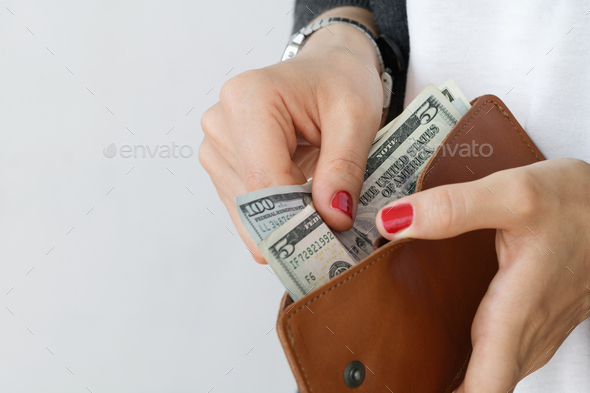 The girl holding an open leather orange slim wallet with cash dollars against white wall.