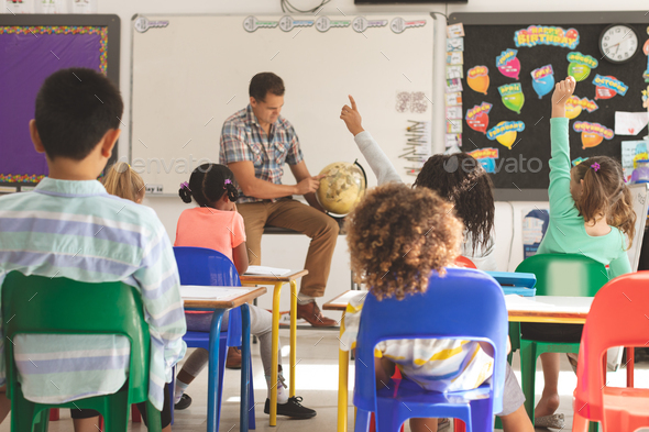 schoolteacher learning at his pupils the earth globe in classroom at school with school kids - Stock Photo - Images