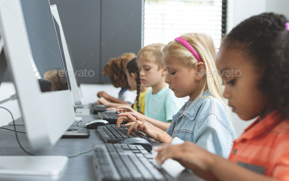 Side view of school kids taping on their keyboard in a computer room at ...