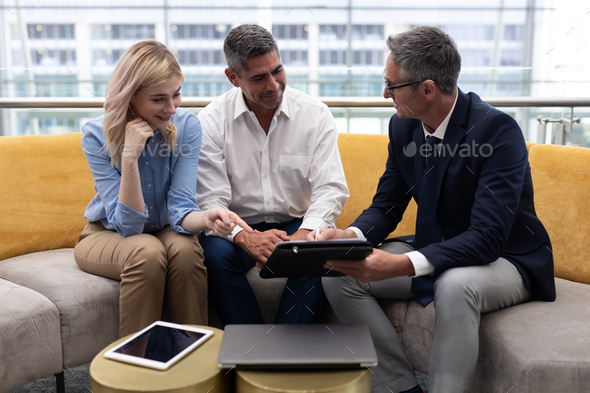Business executives discussing over digital tablet sitting on the sofa in modern office - Stock Photo - Images