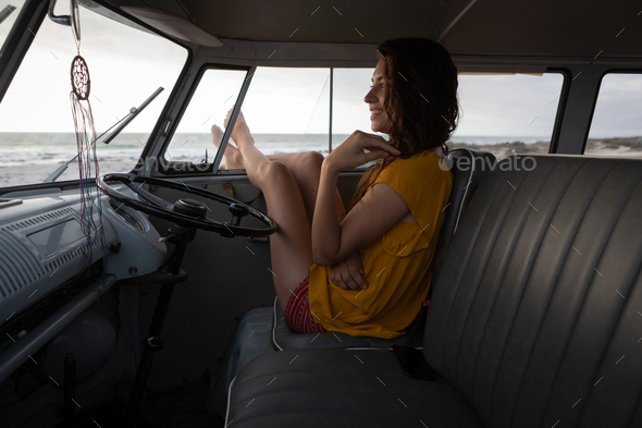 Beautiful woman relaxing in camper van with his foot outside at beach