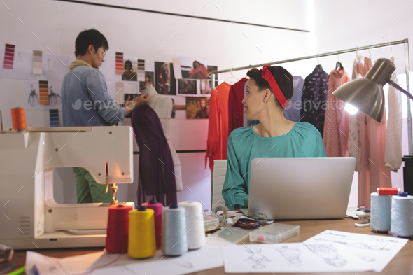 Female fashion designer talking with male designer while working on laptop in design studio