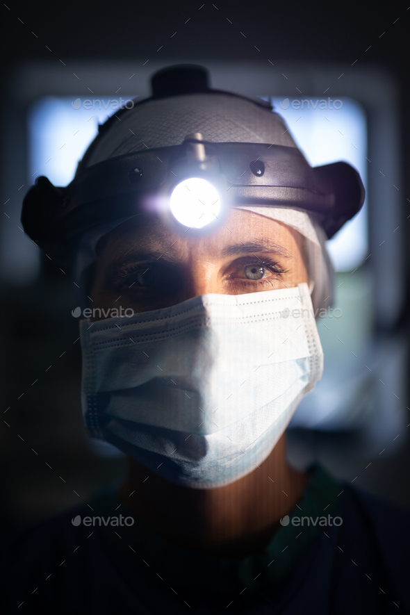 Female surgeon looking at the camera with surgical head lamp on her head in hospital.
